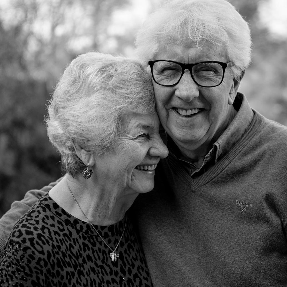 older couple hugging and smiling after receiving dentures to treat missing teeth