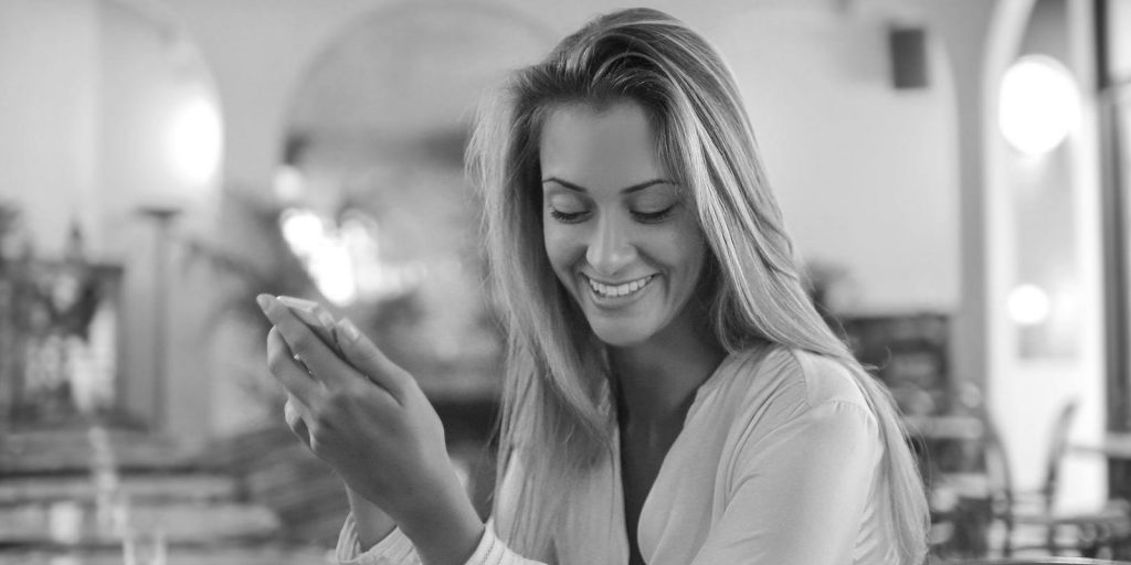 woman smiles whilst holding phone after receiving cosmetic dentistry treatment